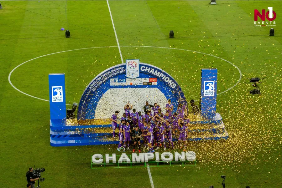Al Ain lifting the ADNOC Pro League trophy on a lit podium amid gold confetti