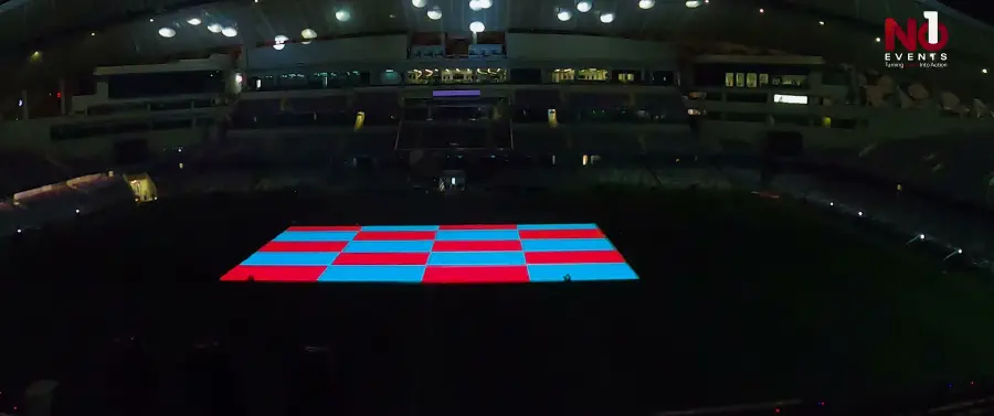 A blacked-out stadium with a red and blue test grid projected onto the pitch