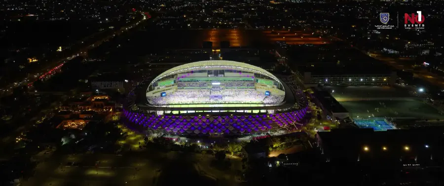 Hazza bin Zayed Stadium lit from outside at night, its roof and facade glowing purple