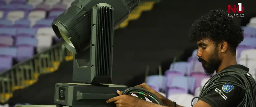 A technician focusing a moving-head fixture positioned in the stadium seating bowl