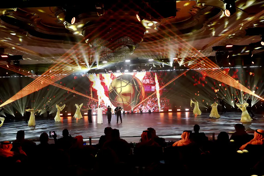 Dancers on the LED floor beneath red and gold beams with content filling the main screen