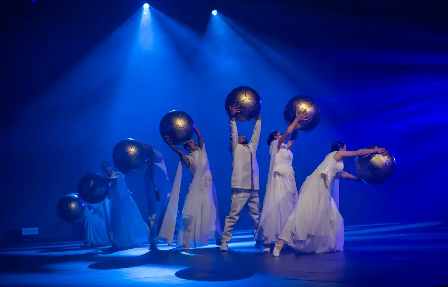 Dancers lifting illuminated globes on a deep blue stage